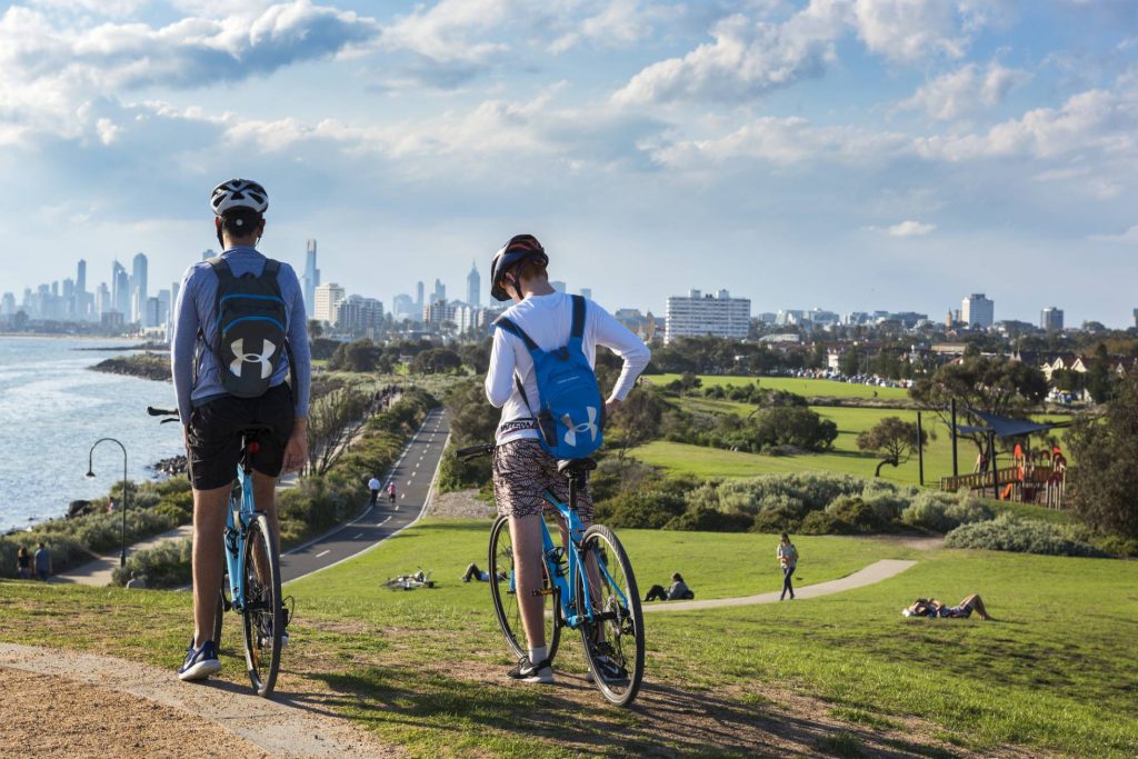 Dois ciclistas em Point Ormond, com o skyline de Melbourne ao fundo. Foto: Christopher Groenhaut / Getty Images. 
