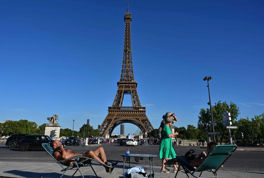 104036943 topshot passers by walk past two people enjoying the sun in a long chair in front of the